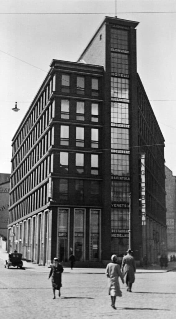 Historiakuva 1930-luvulta Kaisaniemenkatu 13 kiinteistöstä. Muutamia ajan hengen mukaan pukeutuneita ihmisiä kävelee kadulla.